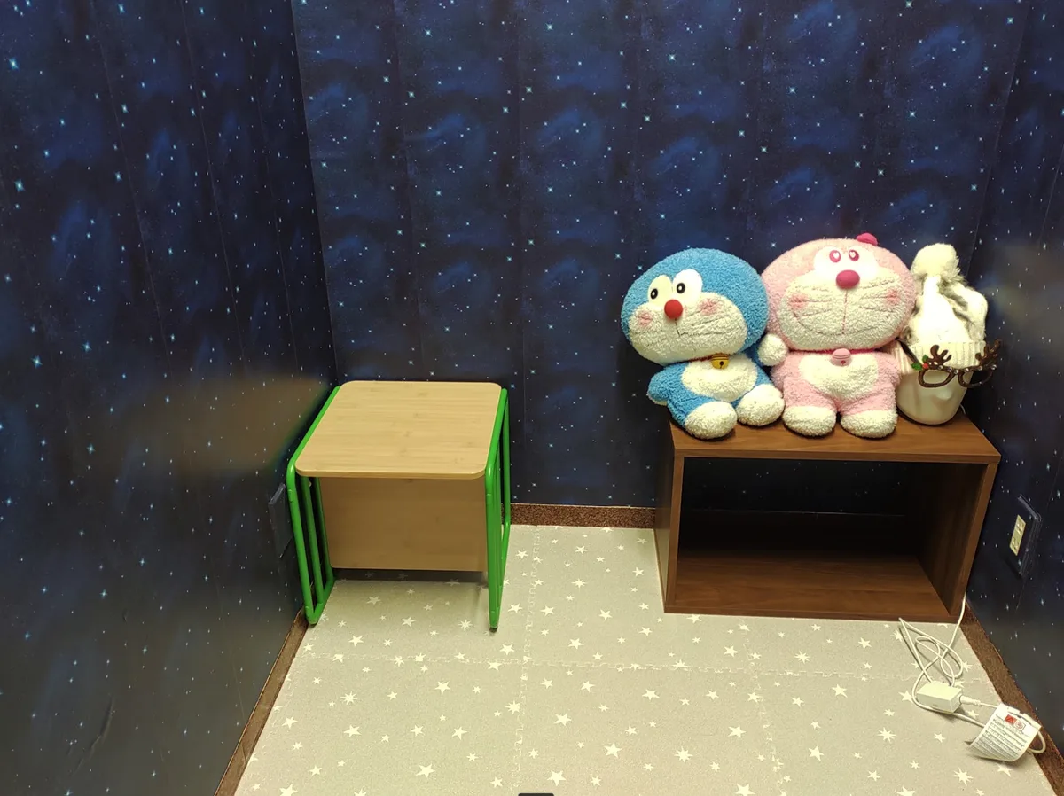 おこもり部屋の中。壁は一面の星空、床は星もようのマット。ぬいぐるみが置かれた棚と小さな机がある