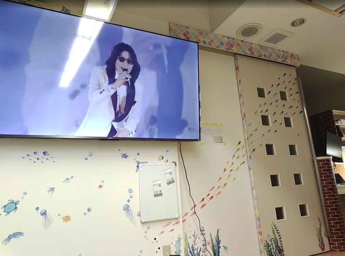 海の生きものが描かれた壁。魚・くらげ・かめの絵が泳ぎ、大きなテレビが取りつけられている